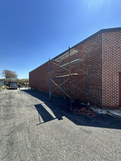 Scaffolding staged along the brick side elevation of an operating warehouse in Hicksville
